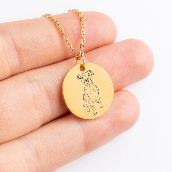 A hand holds the Dog Portrait Necklace - Coin Necklace, a gold round custom piece engraved with a dogs line drawing—an ideal unique accessory for pet lovers.