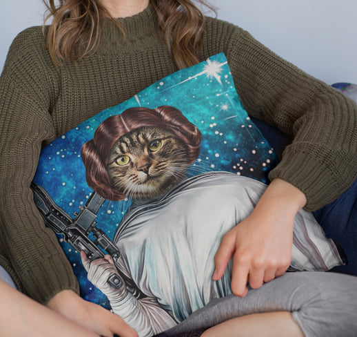 A person in a green sweater holds a Custom Star Wars Princess Leia Pet Cushion featuring a cat as Leia with buns and blaster, set against a starry background—an ideal gift for pet lovers.