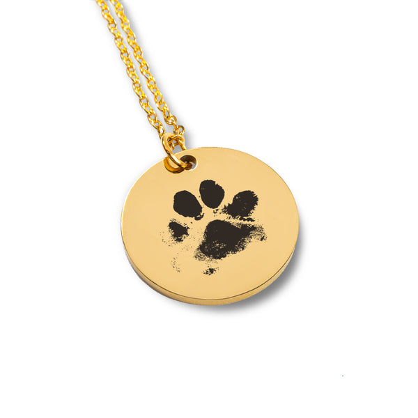 The Dog Paw Necklace - Coin Necklace is a gold pendant with a black paw print on a shiny round disc, ideal as a custom pet necklace and thoughtful gift for pet lovers, shown on a white background.