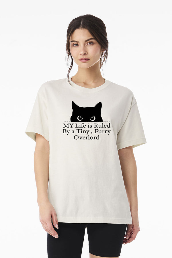 A woman in the Tiny Furry Overlord t-shirt, featuring a black cat face and the phrase MY Life is Ruled By a Tiny, Furry Overlord, stands against a plain white background—a hilarious pet tee for any cat lover.