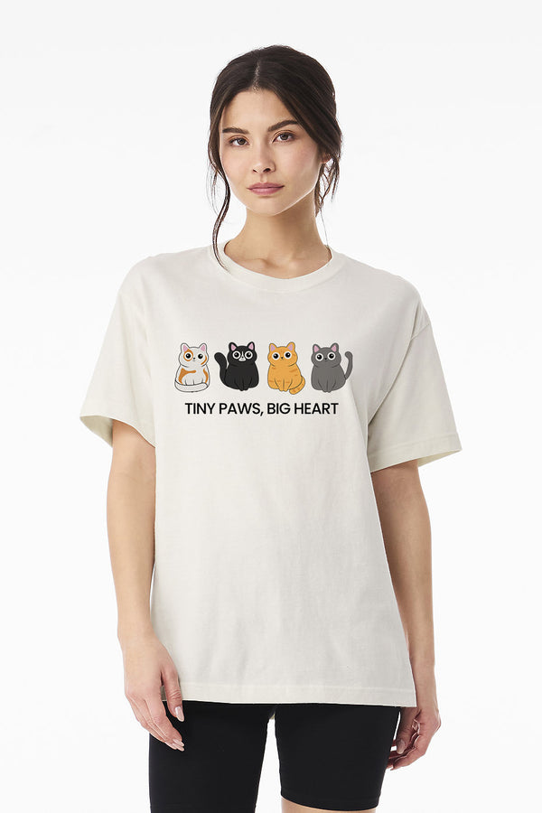 A woman wears the Tiny Paws, Big Heart vintage pet t-shirt with four illustrated cats and the slogan. This funny cat shirt makes a perfect gift for pet lovers. She stands in front of a plain white background.