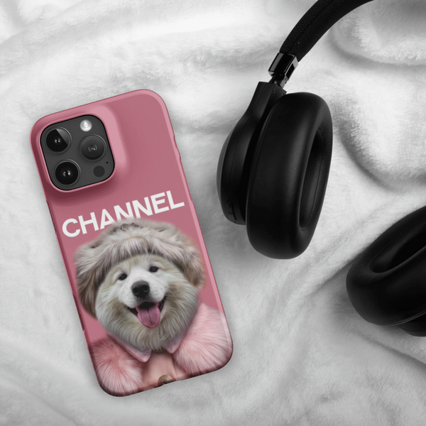 A Custom Pet iPhone Case – Channel Fashion, featuring a smiling dog in a fur coat and hat with the word “CHANNEL,” rests beside black over-ear headphones on a soft white fabric background.