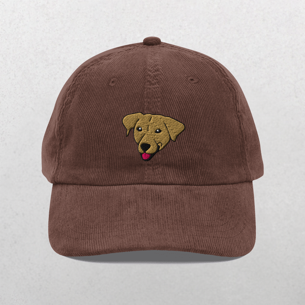 The Custom Pet Portrait Corduroy Cap – Embroidered Pet Hat in brown features an embroidered yellow dog face with its tongue out, centered on the front, set against a plain light gray background.