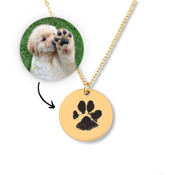 The Dog Paw Necklace - Coin Necklace features a round gold pendant with a black paw print, shown beside a fluffy dog photo—an adorable personalized pet jewelry piece and unique accessory for any pet lover.