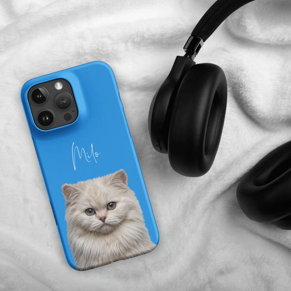 A blue Custom Pet iPhone Case – Modern Vector Art with a fluffy cream cat and the name Milo rests on white fabric beside black over-ear headphones—an ideal pet lover gift.