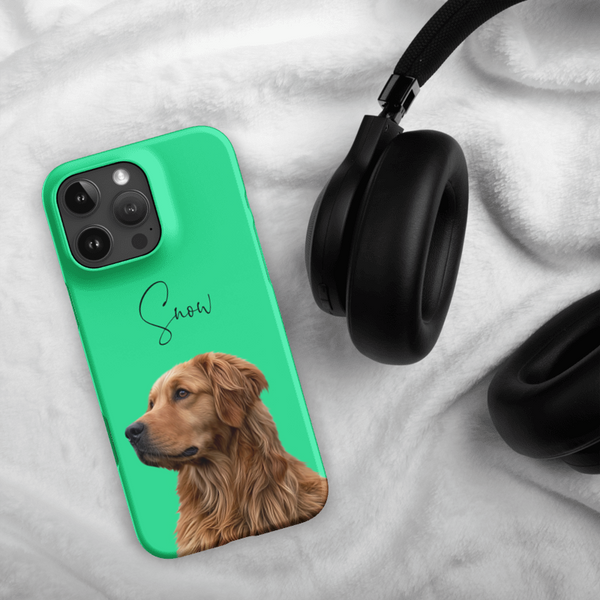 The Custom Pet iPhone Case – Modern Vector Art in green, featuring a golden retriever illustration and the name Snow, sits next to black headphones on a white, fluffy surface—an ideal keepsake for dog lovers.