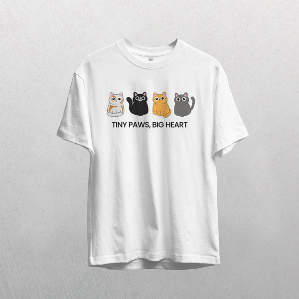 The white Tiny Paws, Big Heart shirt displays four colorful cartoon cats above the slogan, perfect for cat lovers. Shown hanging against a light gray background.