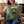 A woman smiles while sitting on a chair, holding the Custom Star Wars Pet Cushion featuring her dog illustrated as a Jedi with a green lightsaber.
