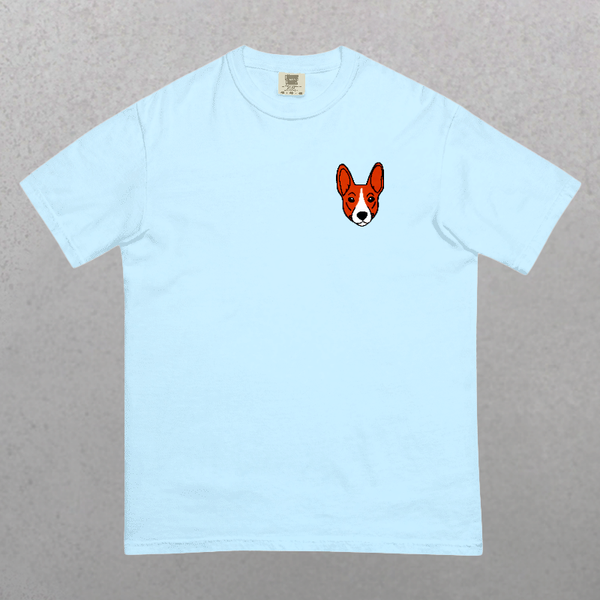 The Embroidered Pet Portrait Organic T-Shirt features a light blue hue with a small, embroidered dog face—orange fur and big ears—on the left chest. Perfect gift for pet lovers, shown laid flat on a neutral background.