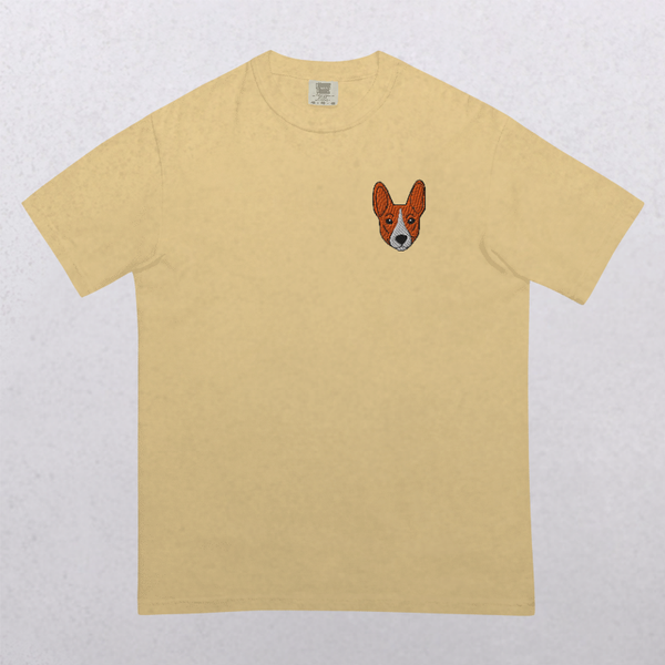 The Embroidered Pet Portrait Organic T-Shirt in beige features a small, embroidered brown and white dog’s face on the left chest—an ideal gift for pet lovers. Shirt shown laid flat on a light, textured background.