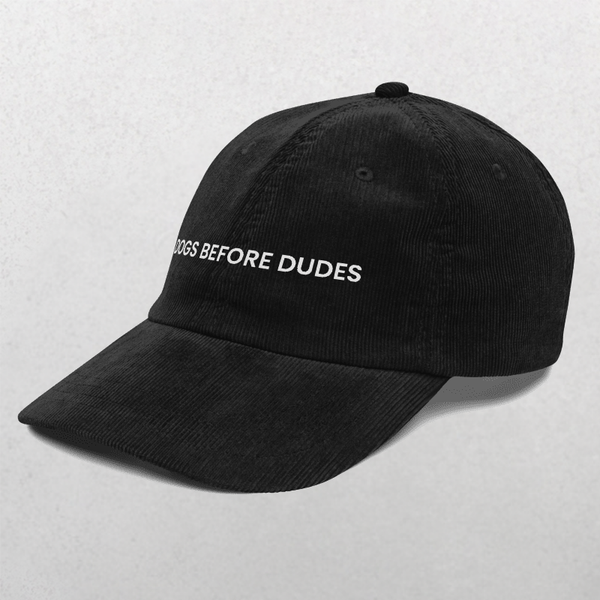 The Chord Vintage Cap - Dogs Before Dudes is a black corduroy baseball cap with DOGS BEFORE DUDES embroidered in white on the front, shown on a light gray background—perfect for trendy dog lovers.
