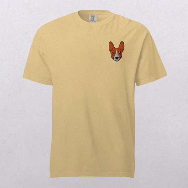 The Embroidered Pet Portrait Organic T-Shirt features a small orange and white cartoon dog face on the left chest, shown on a light gray background—a fun shirt and thoughtful gift for any pet lover.