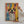 A person hangs the Abstract Masterpiece - Custom Pet Portrait, featuring a happy dog with floppy ears and vibrant blue, yellow, red, and black splashes on a white wall—a perfect gift for pet lovers.