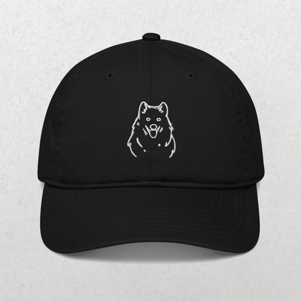 The Embroidered Line art Pet Portrait Organic Classic Dad Cap in black features a white line drawing of a fluffy dog’s face on the front, displayed against a light, textured background.