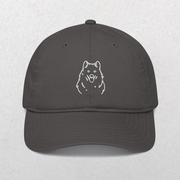 The Embroidered Line Art Pet Portrait Organic Classic Dad Cap in charcoal features a white minimalist dog face on the front—ideal as a personalized pet gift. Photographed on a light, textured surface.