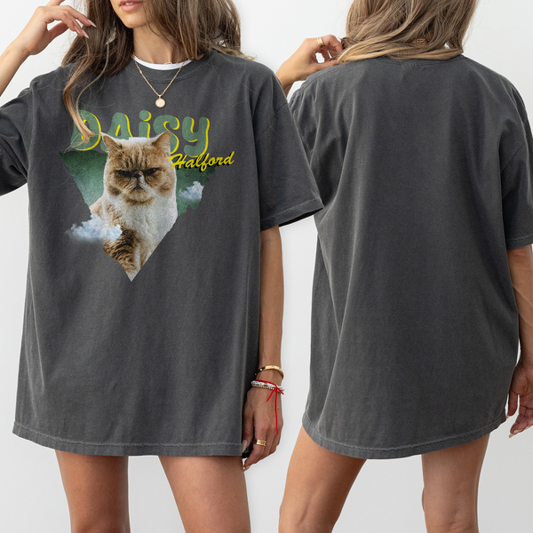 Two women with light brown hair and bracelets wear oversized Personalised Retro Tee | Green shirts featuring a grumpy cat, “Daisy Bradford,” and a green triangle—a unique pet keepsake. The backs are plain.