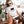 A woman in sunglasses and a Tiny Furry Overlord t-shirt sits on the porch petting her brown and white dog, with a potted plant and beige sofa nearby—an ideal scene for showcasing this fun pet lover tee.