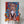 A person in a white shirt holds the Oil Masterpiece - Custom Pet Portrait, featuring a painted brown and white puppy against vibrant blue, orange, and red splashes. Their face is hidden behind this unique pet artwork.