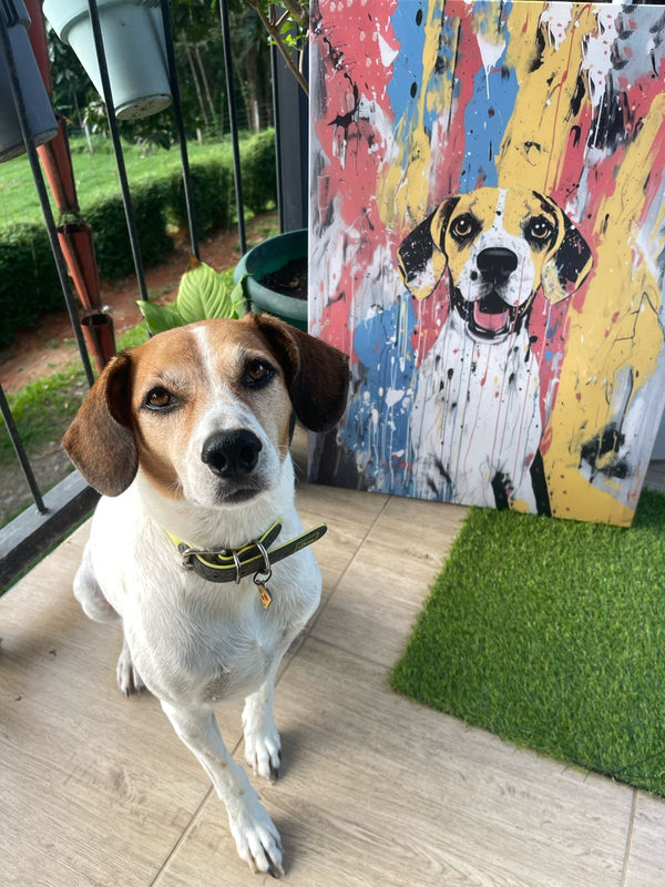 A brown and white dog sits on a patio beside the Abstract Masterpiece - Custom Pet Portrait, a colorful canvas featuring its likeness. Lush plants and green grass are visible in the background.