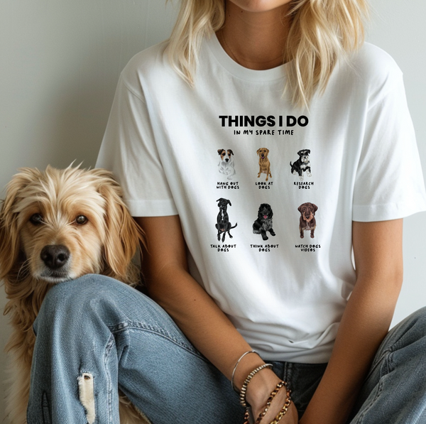 A person wearing the Things I do in my spare time shirt, featuring playful dog illustrations and captions, sits next to a fluffy dog—a perfect gift for pet lovers!.