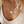 A close-up shows a person in a ribbed cream top wearing the Dog Portrait Necklace - Coin Necklace, featuring a round silver pendant engraved with a floral design. Wavy blonde hair frames this meaningful memorial pet keepsake.