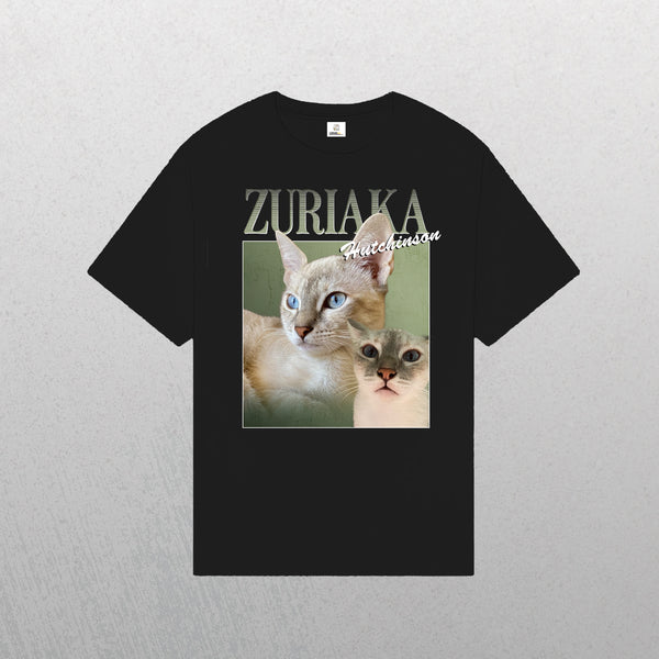 A black Personalised Homage Tee | Jungle, featuring two light-colored cats with blue eyes and ZURIAKA Hutchinson above them. The green background highlights the cats, and the shirt is displayed on a light gray surface.
