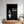 A framed The Dogfather Pet Portrait hangs above a white bed, showing a playful dog in a tuxedo with a red rose, styled like a movie poster. Potted plants sit on a nearby wooden table.