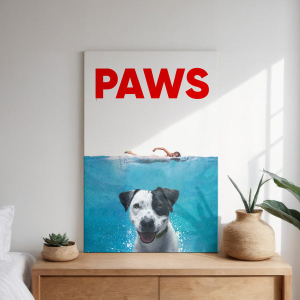 The Paws Film Cover is a framed poster on a wooden dresser, showing a swimmer above water and a smiling dog below. PAWS appears in bold red letters at the top, resembling custom pet portrait wall art, with plants beside the poster.