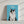 A Disney Pet Portrait canvas features a cartoon-style fluffy black and white cat on a blue background with Milo in white script above, creating a charming pet memorial wall art piece displayed against a wall.